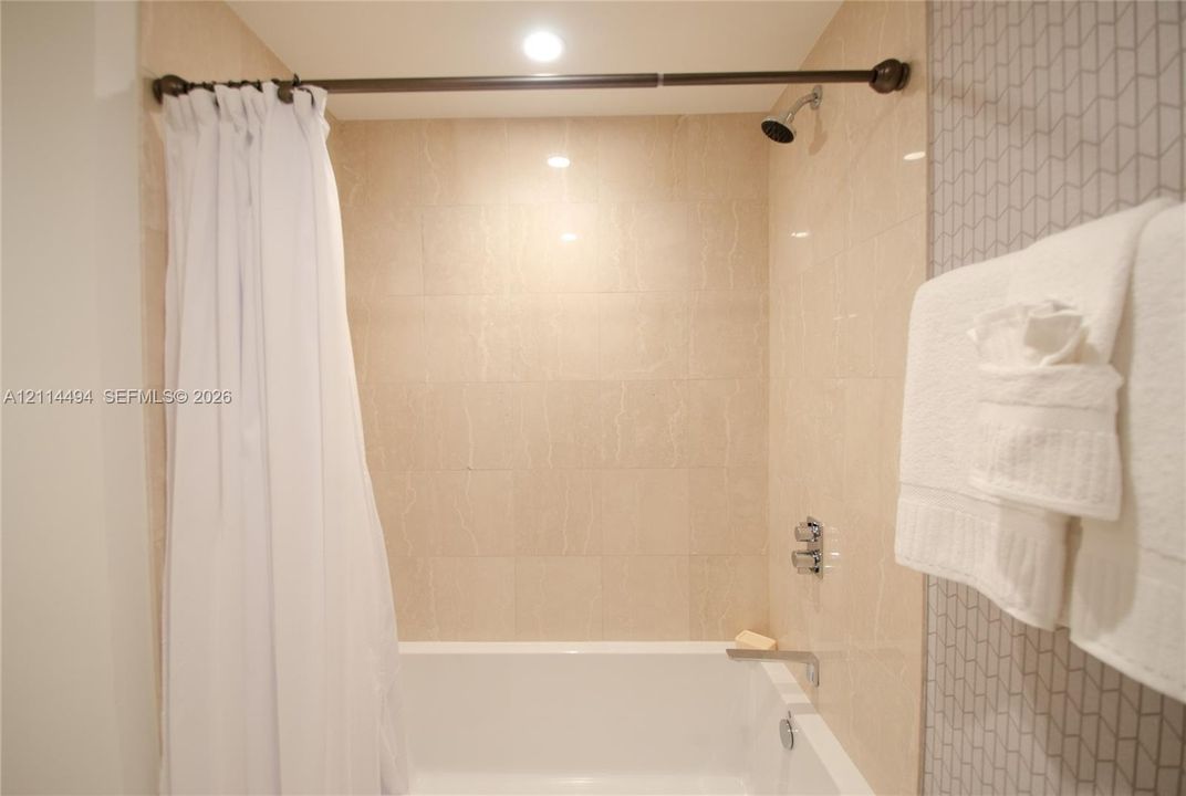 Shower and bathtub combination featuring large-format beige wall tiles, chevron-patterned accent tiling, a chrome wall-mounted shower head, and a chrome tub filler