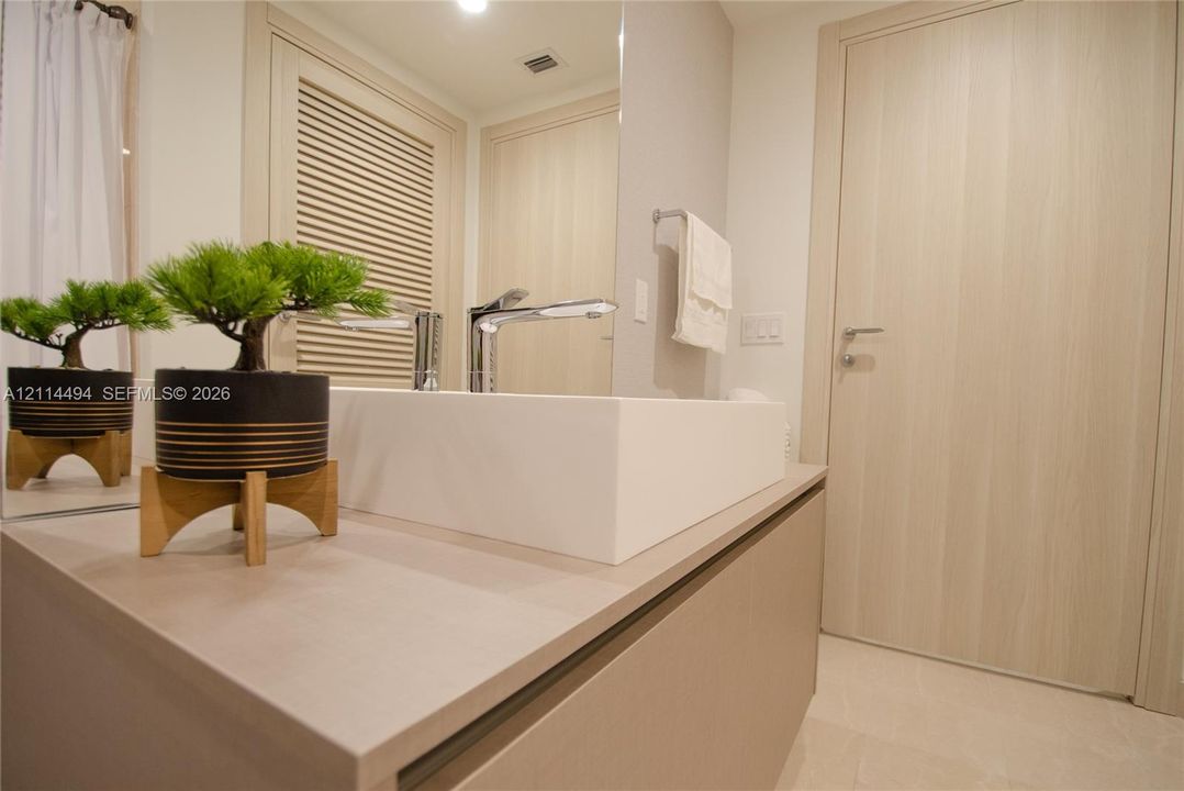 Modern vanity featuring a solid surface countertop, rectangular vessel sink, polished chrome faucet, louvered built-in cabinet doors, and light-toned slab door