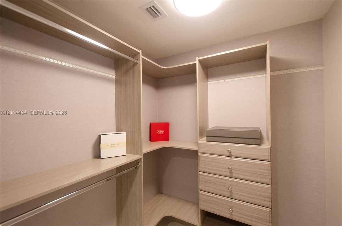 Walk-in closet featuring light wood-finish shelving, integrated hanging rods, and a four-drawer built-in cabinet unit with metallic pulls