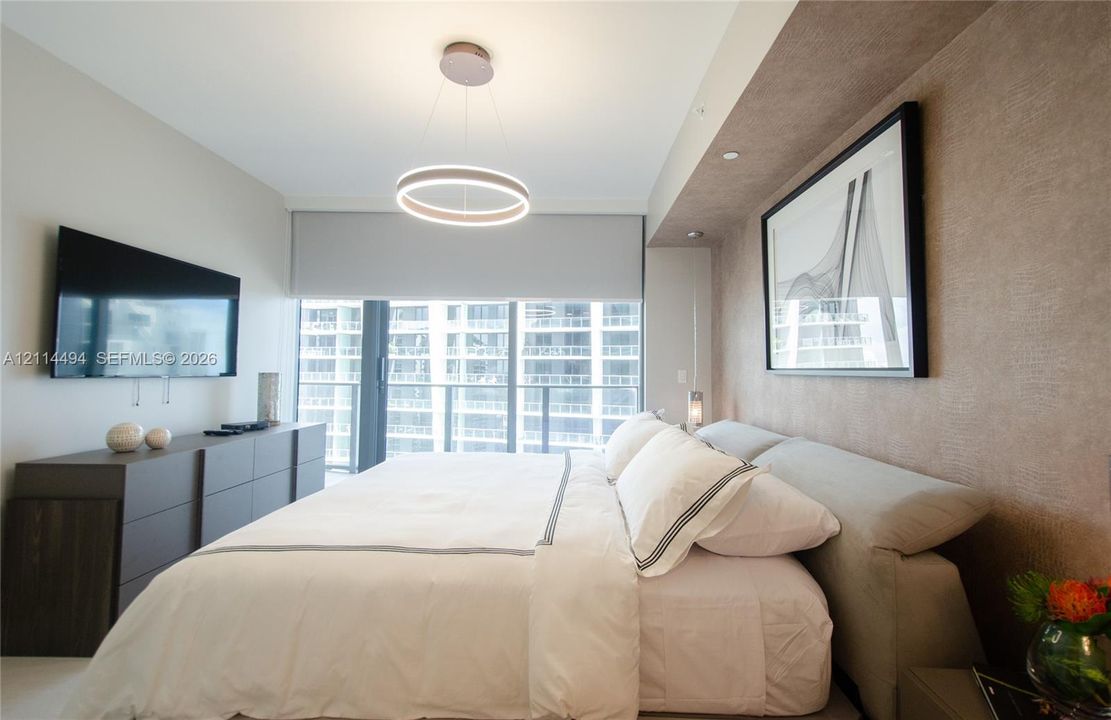 Floor-to-ceiling windows with roller shades, recessed cove lighting, circular LED chandelier, and textured wall finish