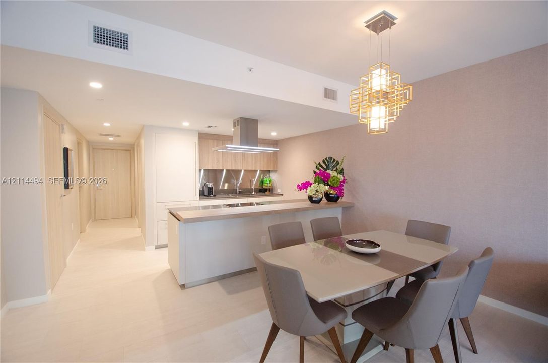 Kitchen featuring a stainless steel range hood, stone-finish countertops, flat-panel cabinetry, geometric pendant lighting, and neutral-tone tile flooring