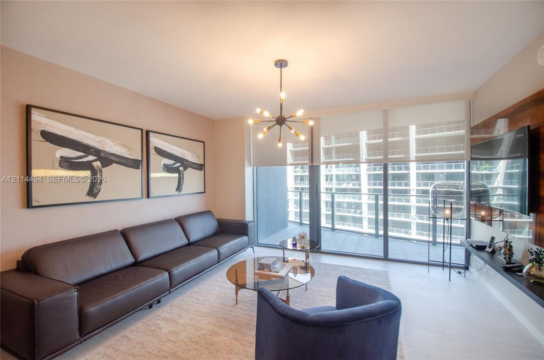 Living area featuring light-toned flooring, floor-to-ceiling glass doors, a contemporary multi-arm sputnik-style chandelier, and a wood-finish wall panel