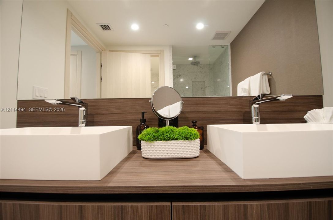 Dual rectangular vessel sinks atop a wood-finish vanity with a matching backsplash, polished chrome faucets, and a large integrated mirror