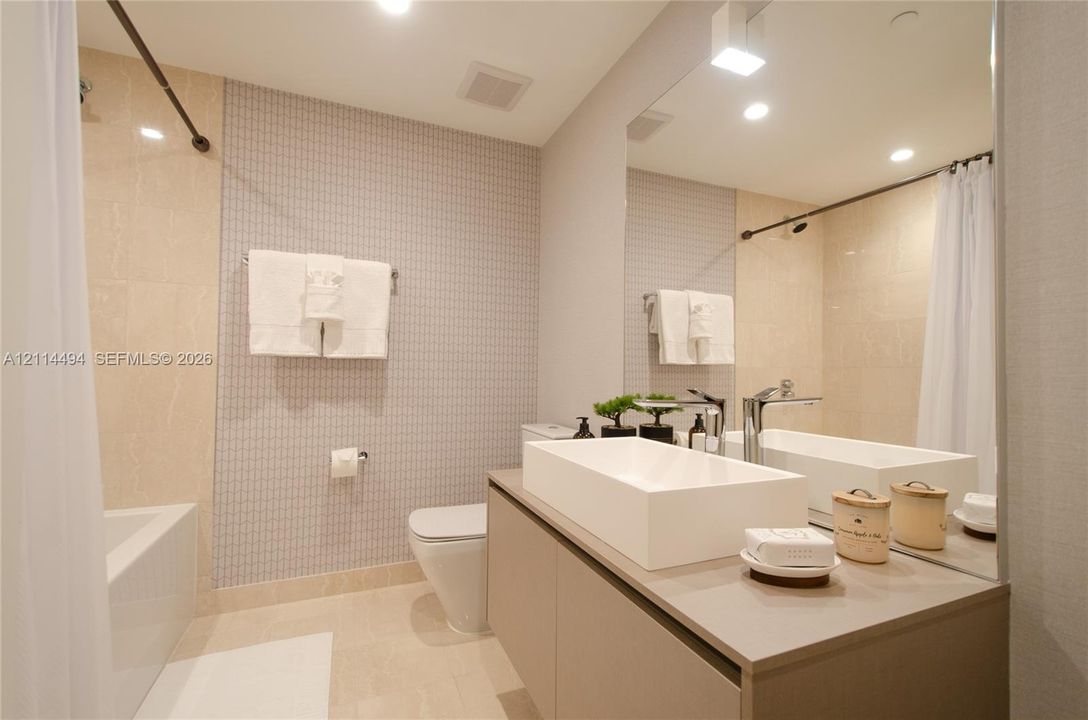 Floating vanity featuring a rectangular vessel sink and polished chrome faucet, paired with a large wall-mounted mirror, mosaic tile wall accents, and a built-in bathtub with shower surround