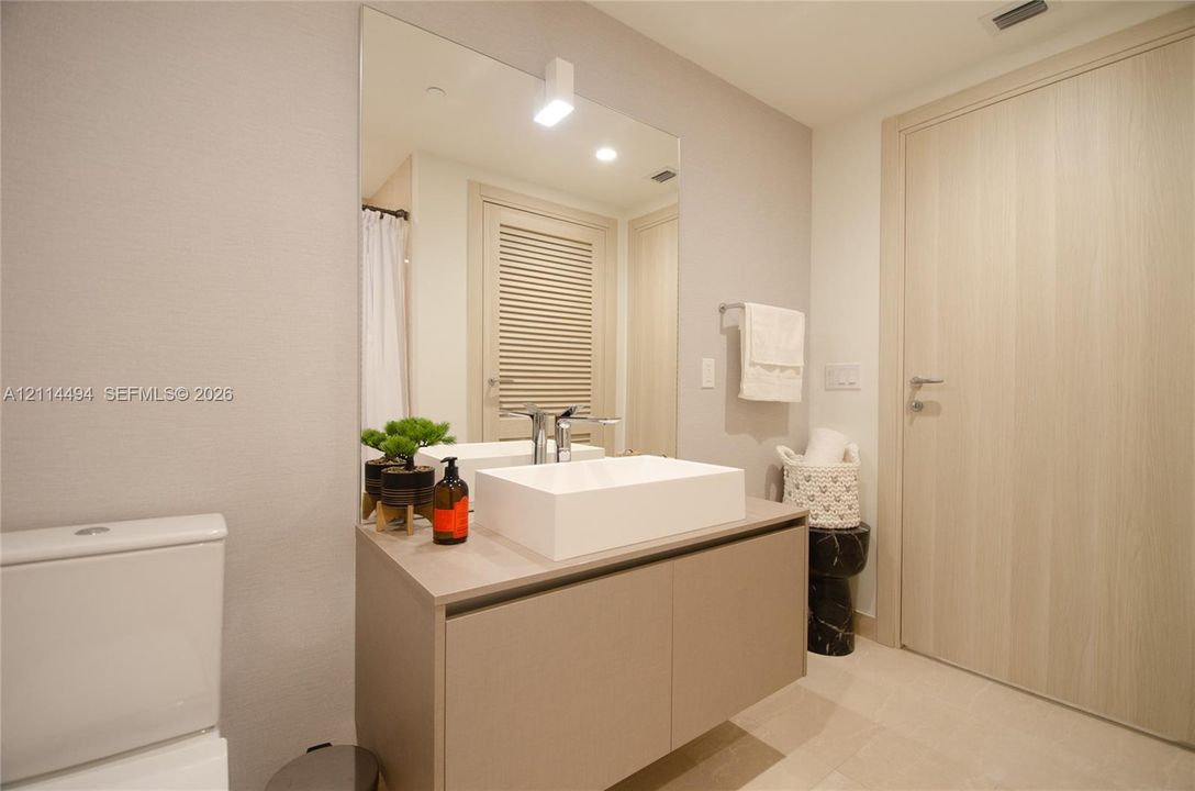 Modern floating vanity with a rectangular vessel sink and wall-mounted faucet, oversized wall mirror, light-toned wood-finish door, and neutral tile flooring