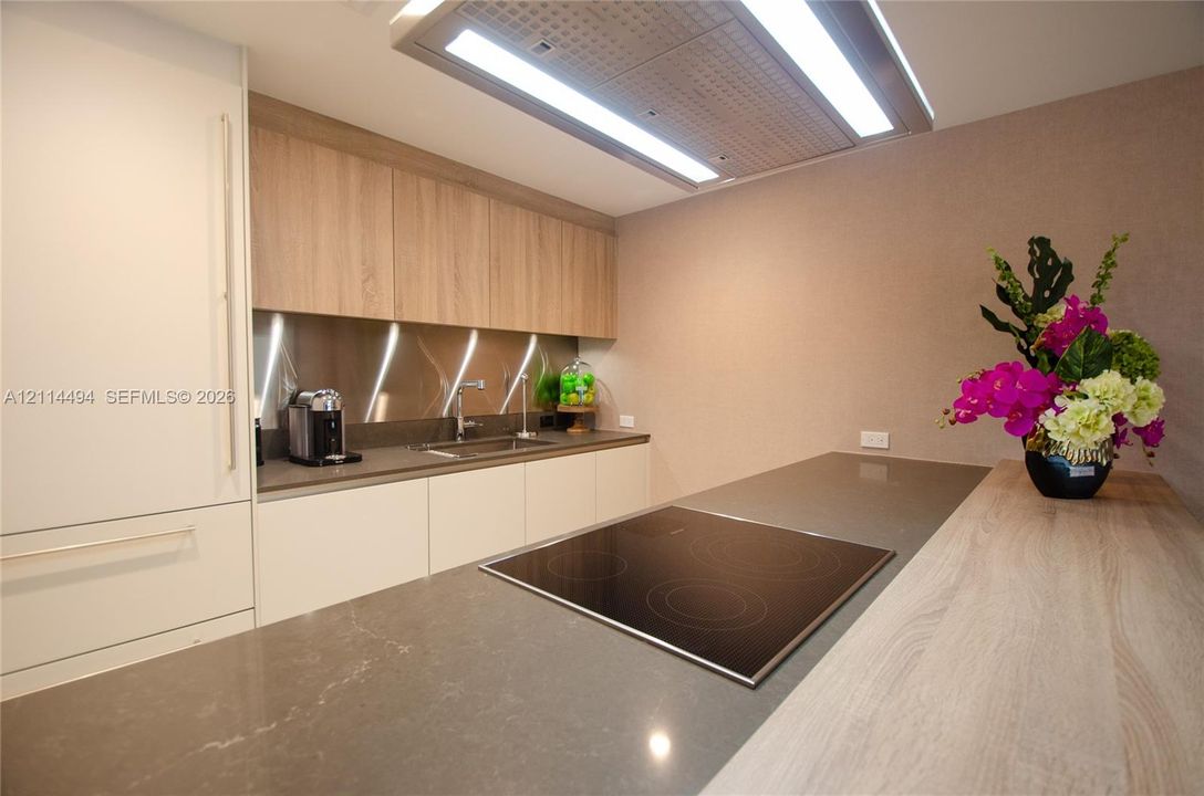 Kitchen featuring flat-panel cabinetry, stone countertops, metallic backsplash, integrated induction cooktop, and flush-mount overhead ventilation