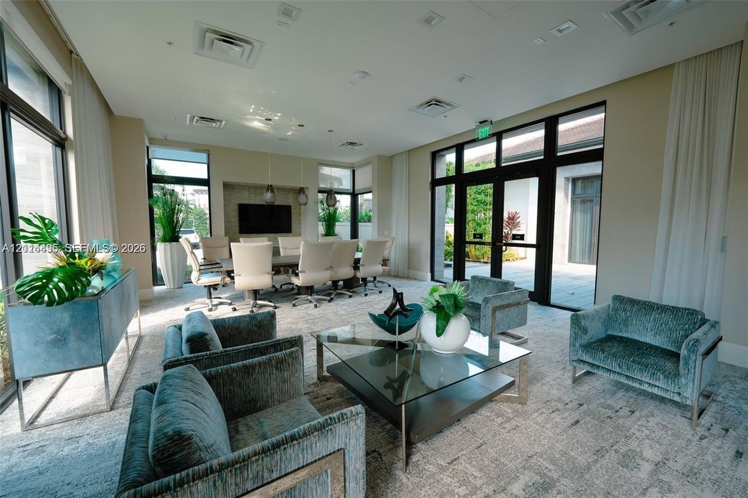 Expansive communal space featuring floor-to-ceiling windows, high-contrast dark window frames, recessed ceiling lighting, and neutral carpeting