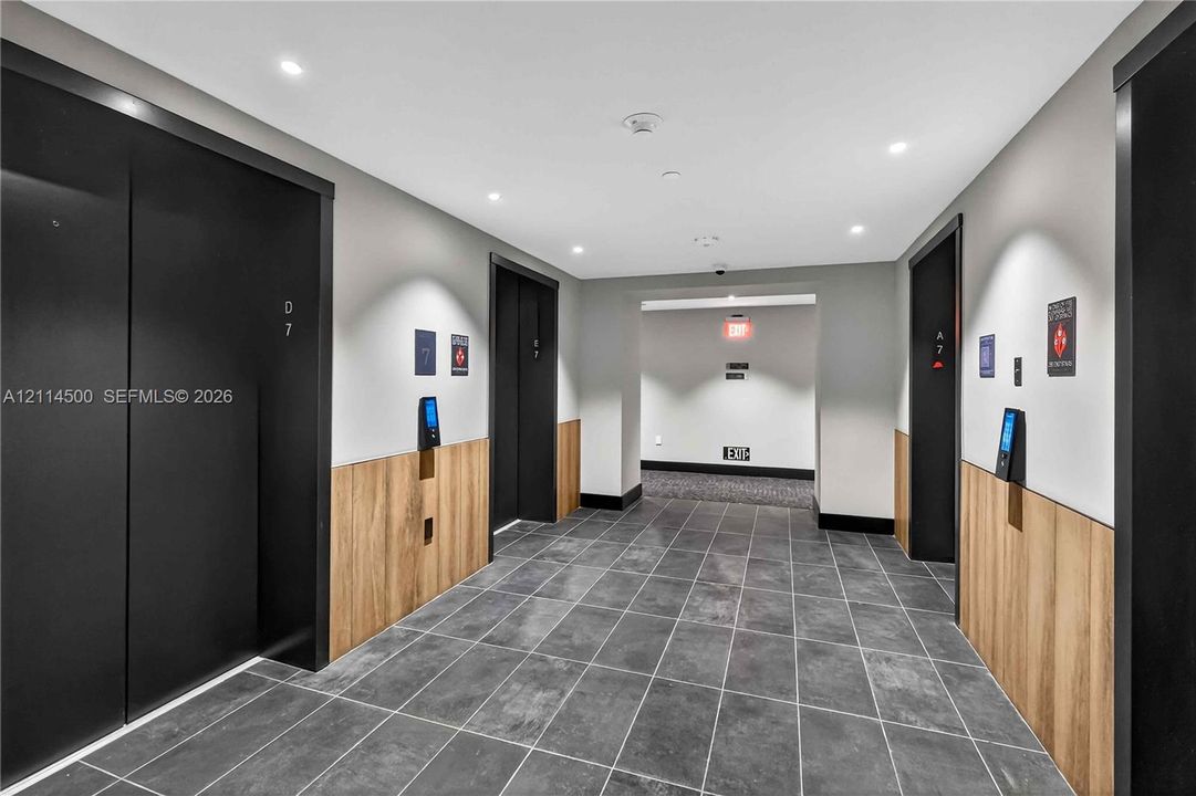 Elevator lobby featuring matte black doors, wood-finish lower wall paneling, large-format tile flooring, and recessed ceiling lighting