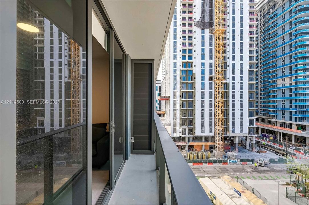 Private balcony featuring floor-to-ceiling glass sliding doors, dark metal railings, and concrete flooring