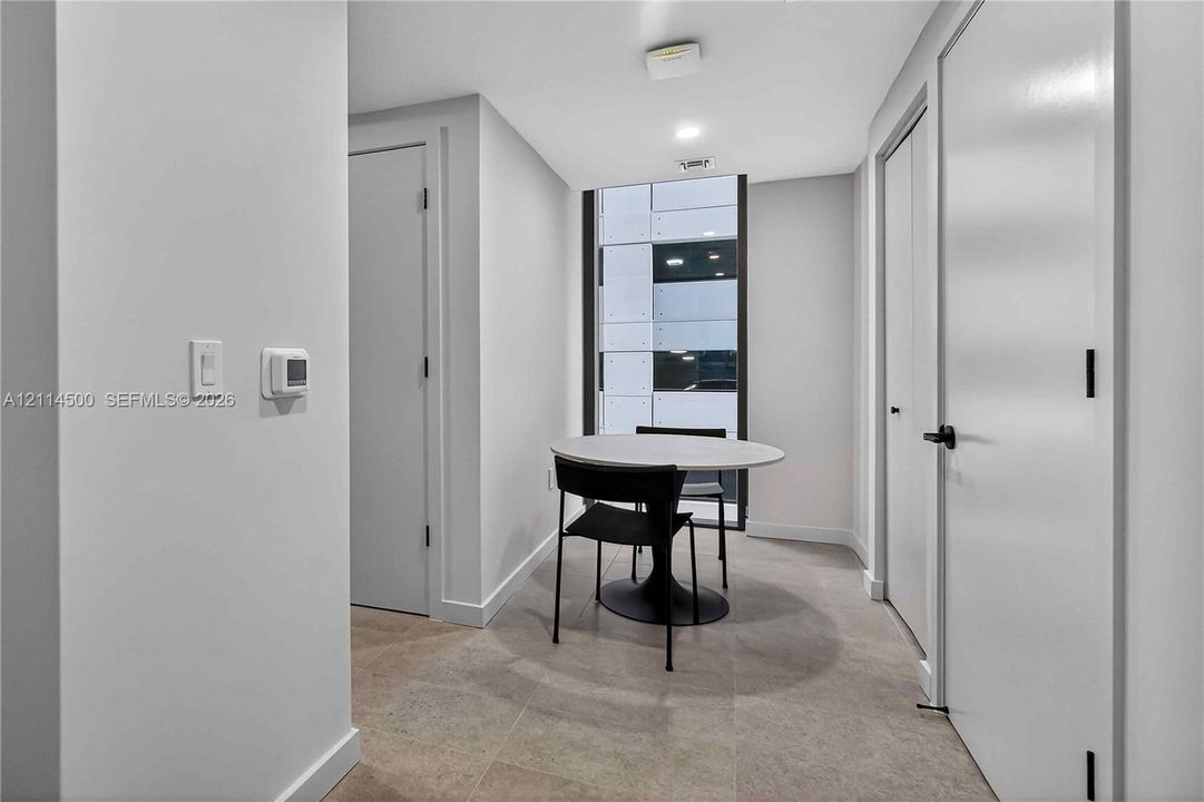 Neutral-toned interior space featuring large floor-to-ceiling windows, tile flooring, and white double-door closet storage with matte black hardware