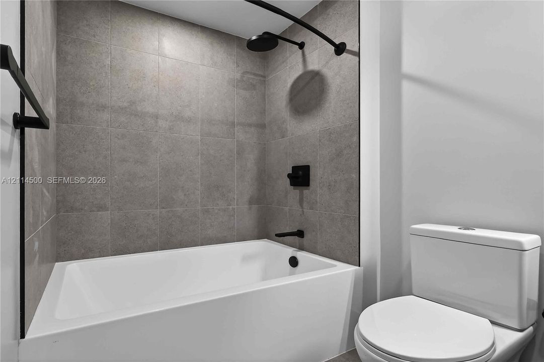 Bathroom featuring a white deep-basin tub, matte black shower head and faucet hardware, and full-height grey tile wall surround