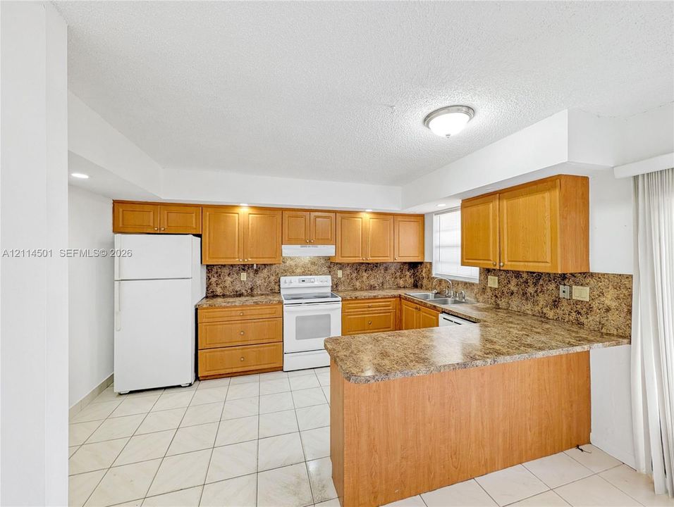 Kitchen featuring wood cabinetry, laminate countertops, a dual-basin sink, white appliances, and ceramic tile flooring