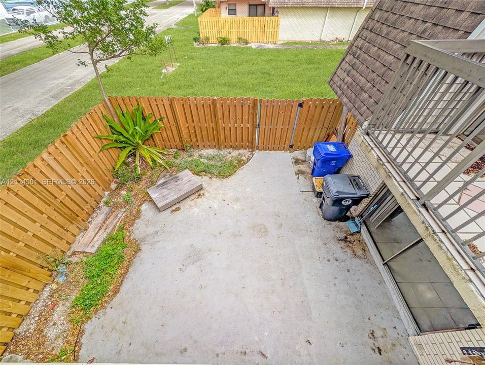 Enclosed courtyard featuring a concrete patio, wood-slat perimeter fencing, and an elevated wooden balcony