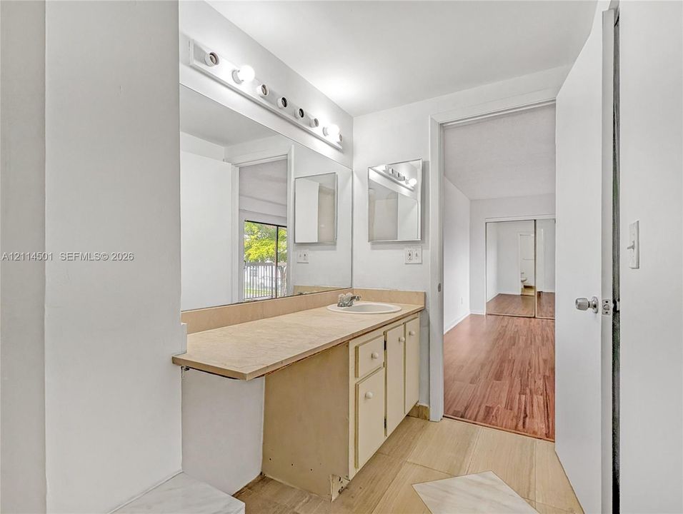 Full-width vanity with countertop basin, integrated cabinetry, large wall-mounted mirror, overhead multi-bulb lighting, and tile flooring