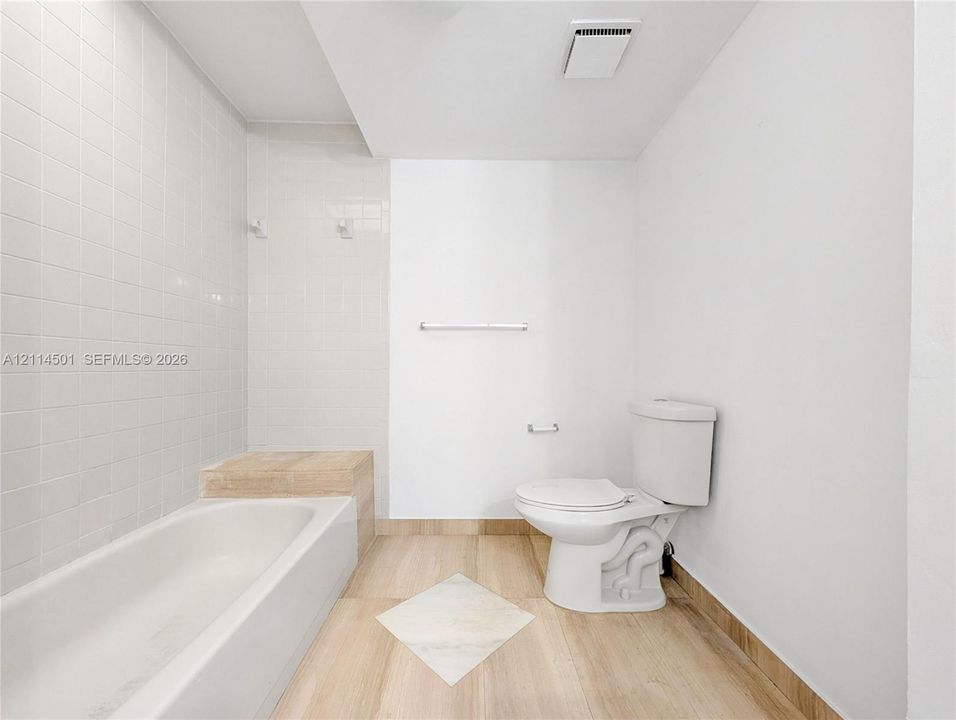 Full-size soaking tub featuring a neutral tile surround, wood-finish flooring, and minimalist wall-mounted hardware