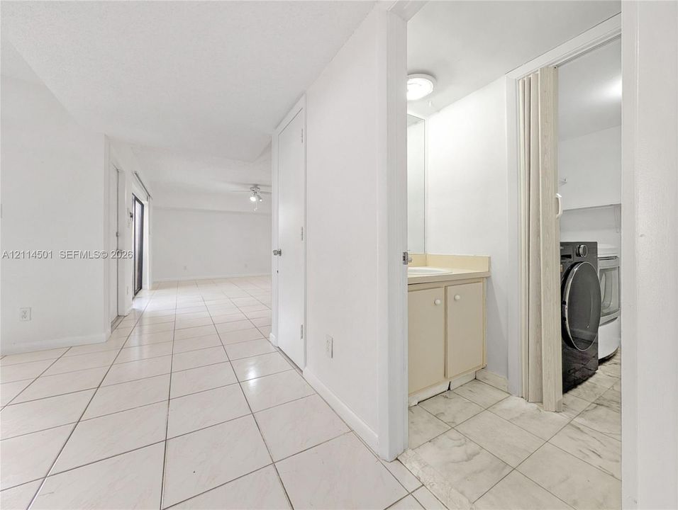 Interior hall featuring large-format ceramic tile flooring, built-in vanity with integrated countertop, and laundry area enclosed by accordion doors