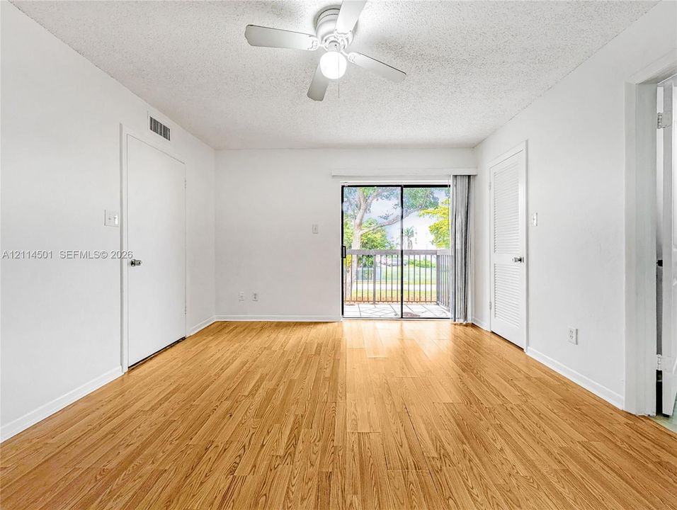 Wood-finish flooring, ceiling fan with integrated lighting, and sliding glass doors opening to a private balcony
