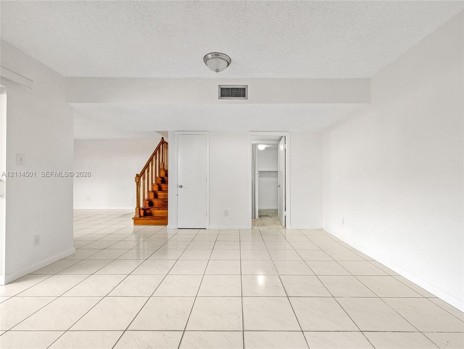 Neutral-toned tile flooring, flush-mount ceiling lighting, and a wood-stain staircase with a banister