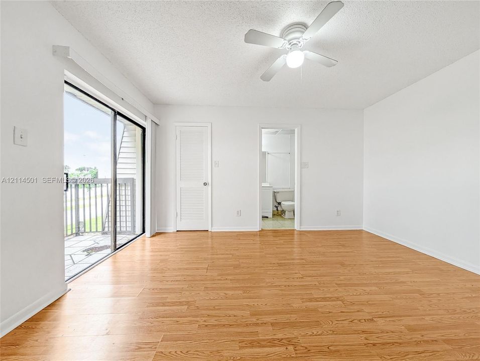 Wood-finish flooring, sliding glass door with balcony access, ceiling fan with integrated lighting, and louvered closet door