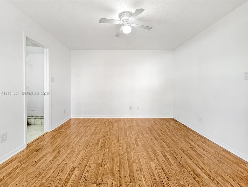 Room featuring wood-finish flooring, white walls, and a ceiling fan with integrated lighting