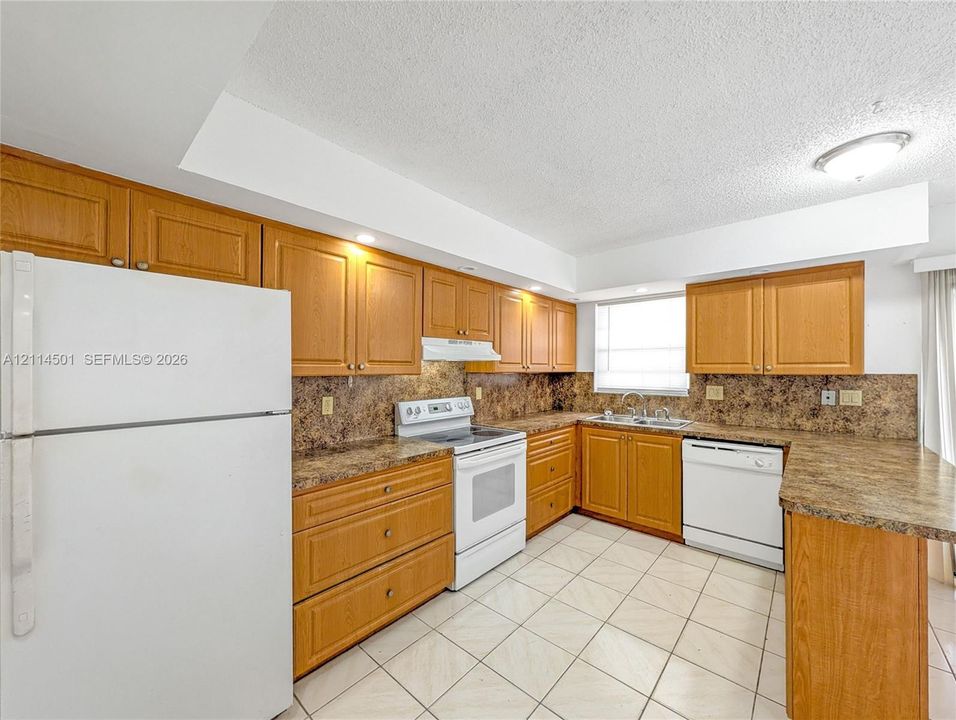 Kitchen featuring wood cabinetry, laminate countertops, a tile backsplash, white appliances, and tiled flooring