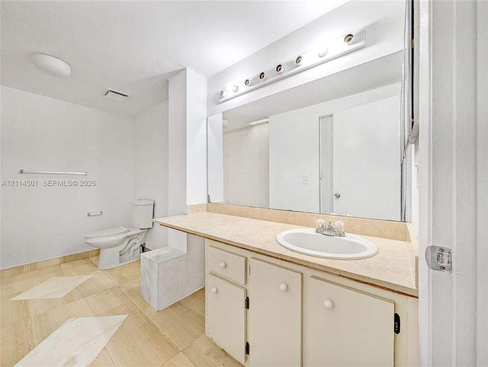 Large wall-mounted mirror, vanity featuring light-toned cabinetry and a solid-surface countertop with an integrated oval sink, and tile flooring