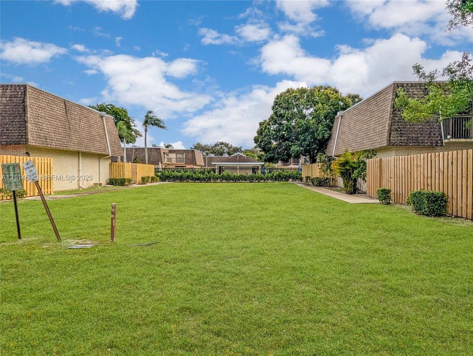 Expansive common area featuring a manicured lawn, perimeter wood fencing, and established landscaping