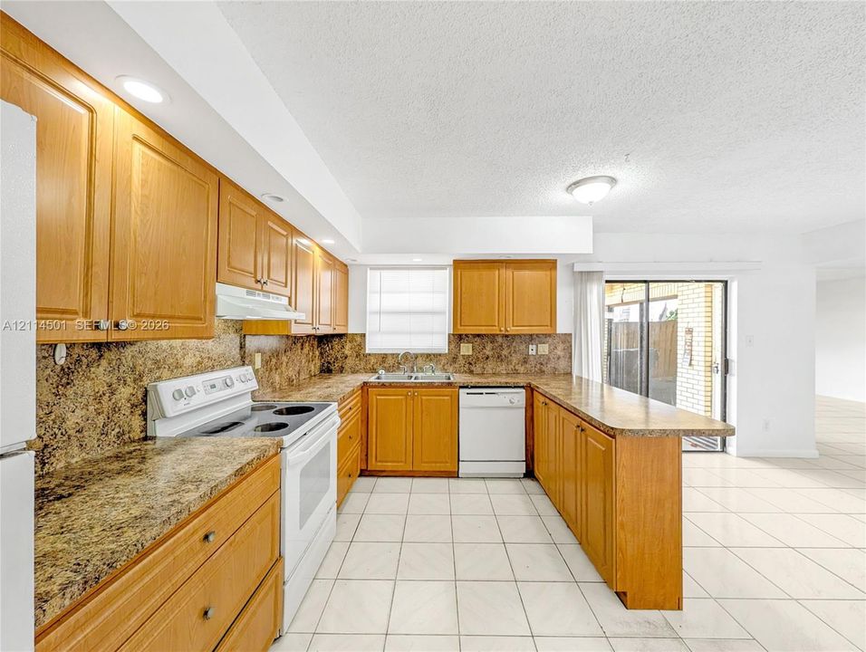 Kitchen featuring wood cabinetry, stone-finish countertops, tile flooring, recessed ceiling lighting, and a peninsula configuration