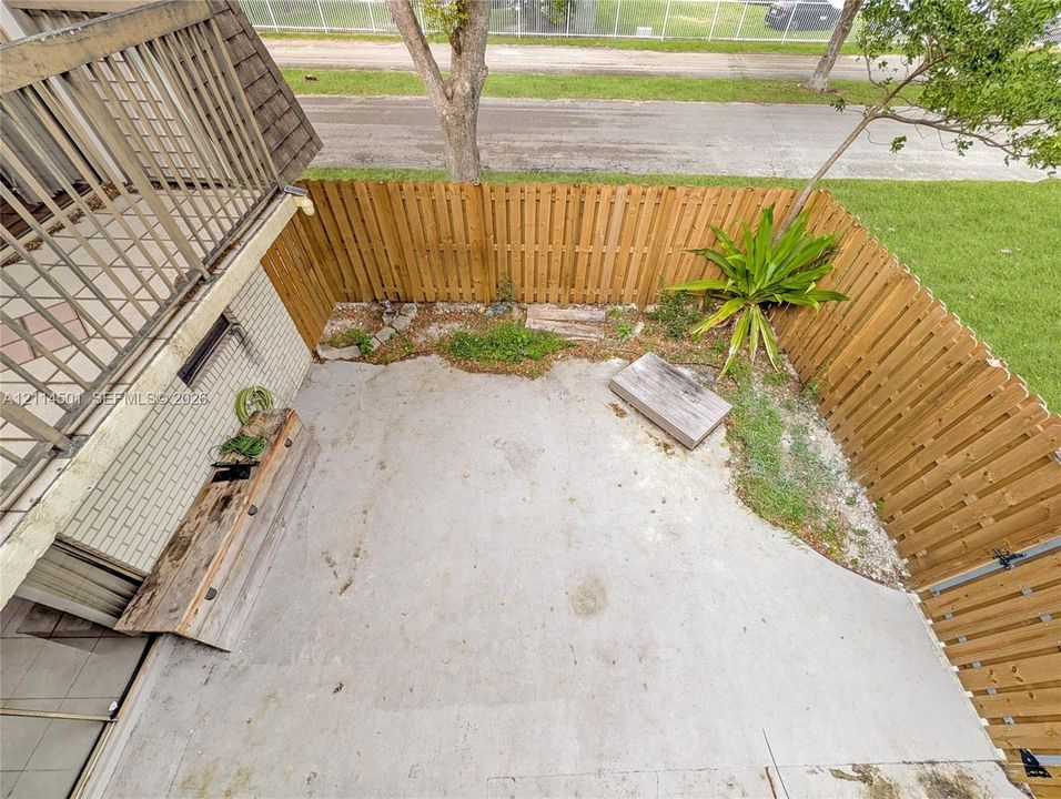 Private courtyard featuring a concrete patio, perimeter wood fencing, and an elevated balcony above