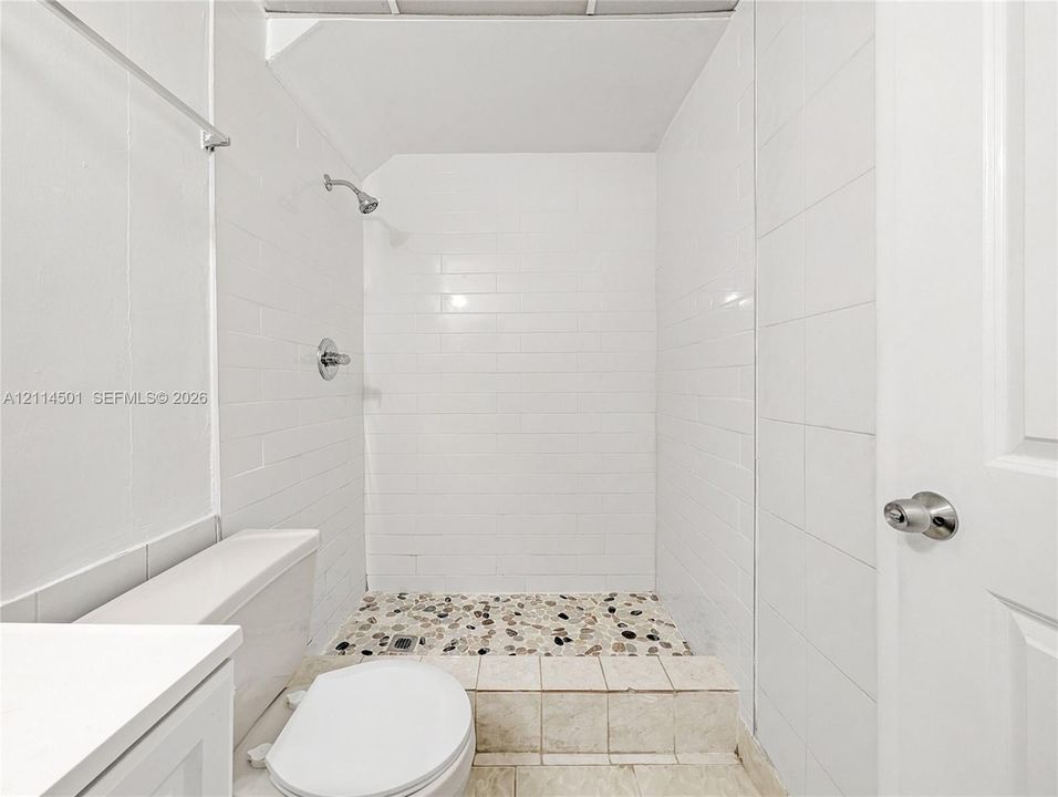 Walk-in shower with white subway tile surround, pebble stone flooring, raised threshold, and metallic wall-mounted shower fixture