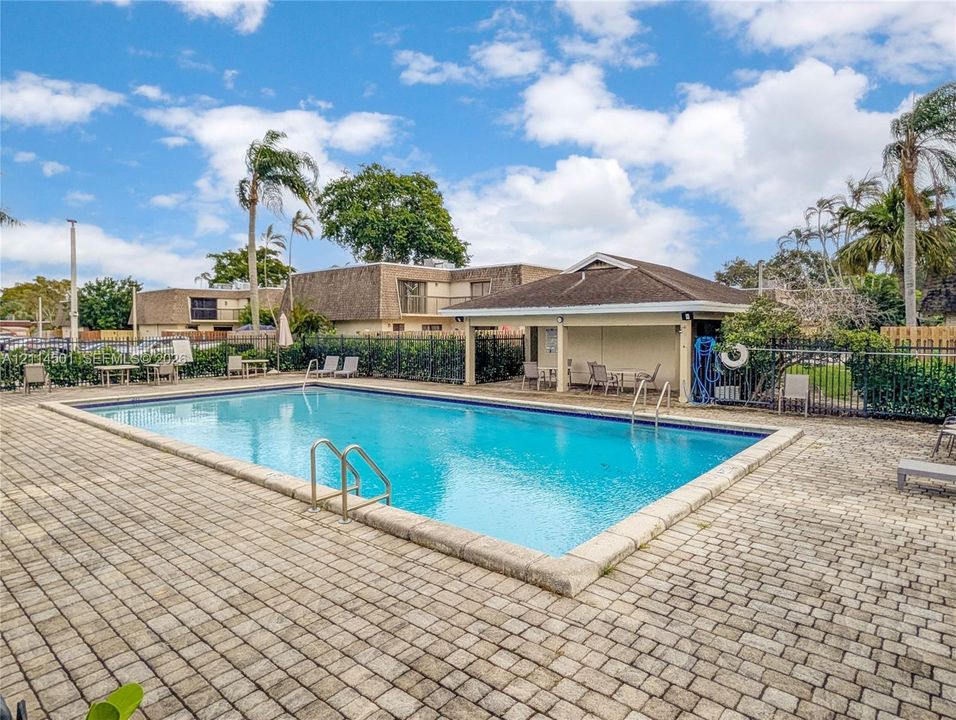 Rectangular swimming pool featuring stone paver decking, metal perimeter fencing, and an open-air covered pavilion