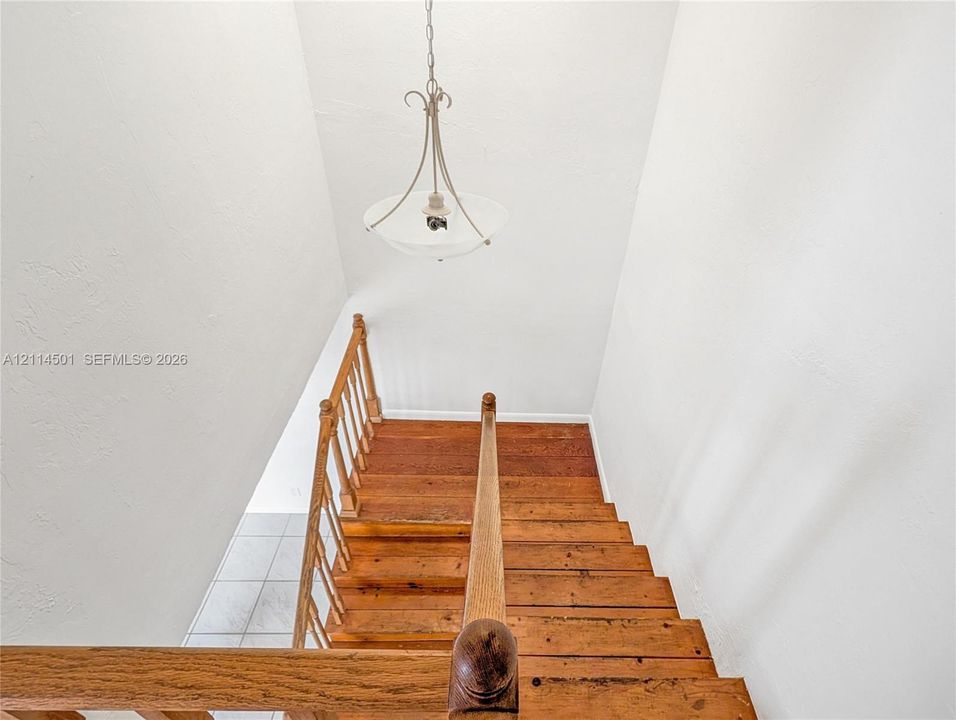 Staircase featuring natural wood-finish treads, matching wooden handrail with a decorative newel post, and a suspended pendant light fixture