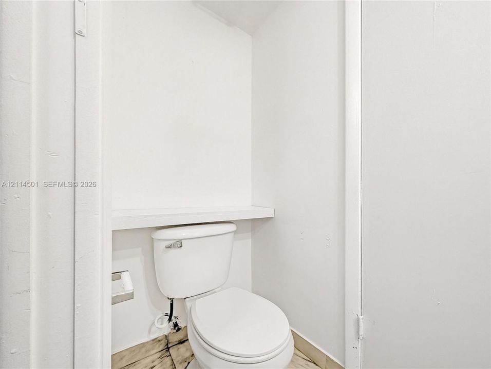 White toilet with a built-in recessed shelf and metal toilet paper holder atop natural stone flooring