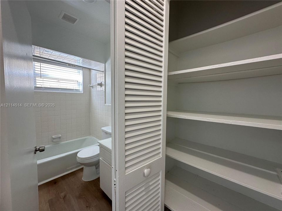 Bathroom featuring a built-in linen closet with louvered doors, white tiled walls, a bathtub with a shower surround, a white vanity, and wood-finish flooring