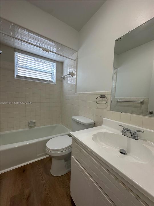 Bathroom featuring a white vanity with an integrated basin, wood-finish flooring, tiled shower surround, and a recessed mirror