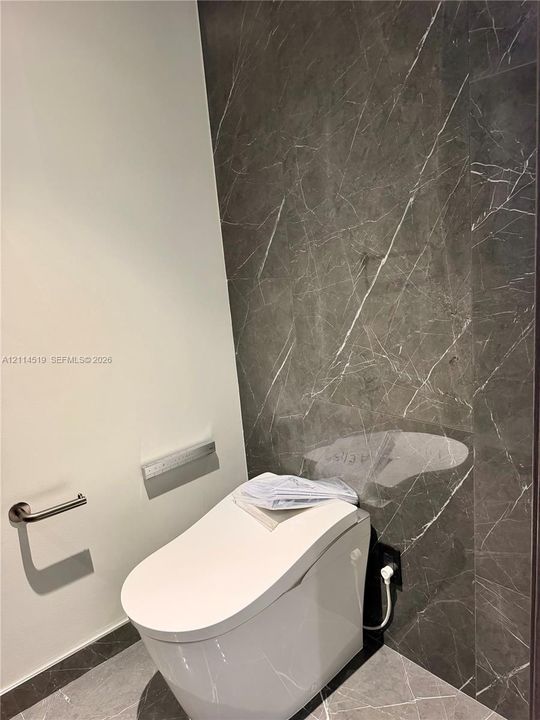 Modern restroom featuring full-height charcoal-toned stone wall cladding, matching stone floor tile, and a contemporary low-profile toilet with integrated flush system and brushed nickel hardware