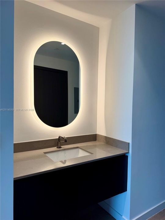Floating vanity with stone countertop, undermount sink, metallic faucet, and oval back-lit mirror