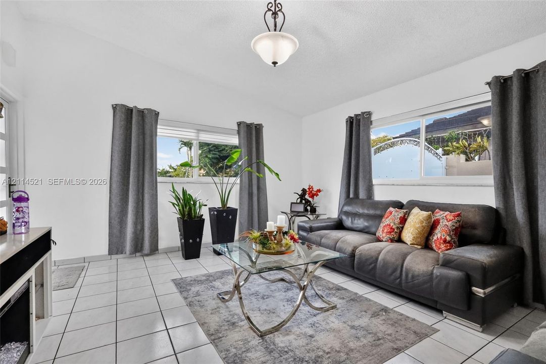 Living area featuring light-toned ceramic tile flooring, vaulted ceilings, dual-pane windows, and a central pendant light fixture