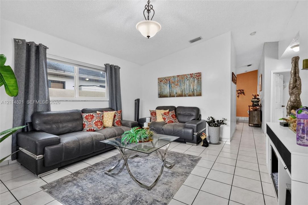 Living area featuring light-colored floor tiling, a single-hung window, and a central pendant light fixture