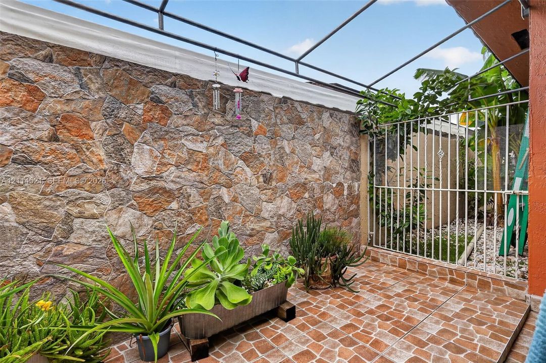Enclosed patio featuring a natural stone accent wall, tiled flooring, and a metal pergola frame