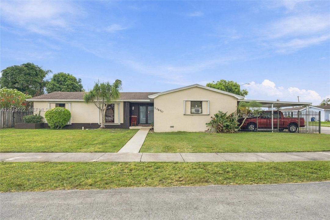Single-story residence featuring a stucco exterior, integrated carport, concrete walkway, and perimeter metal fencing