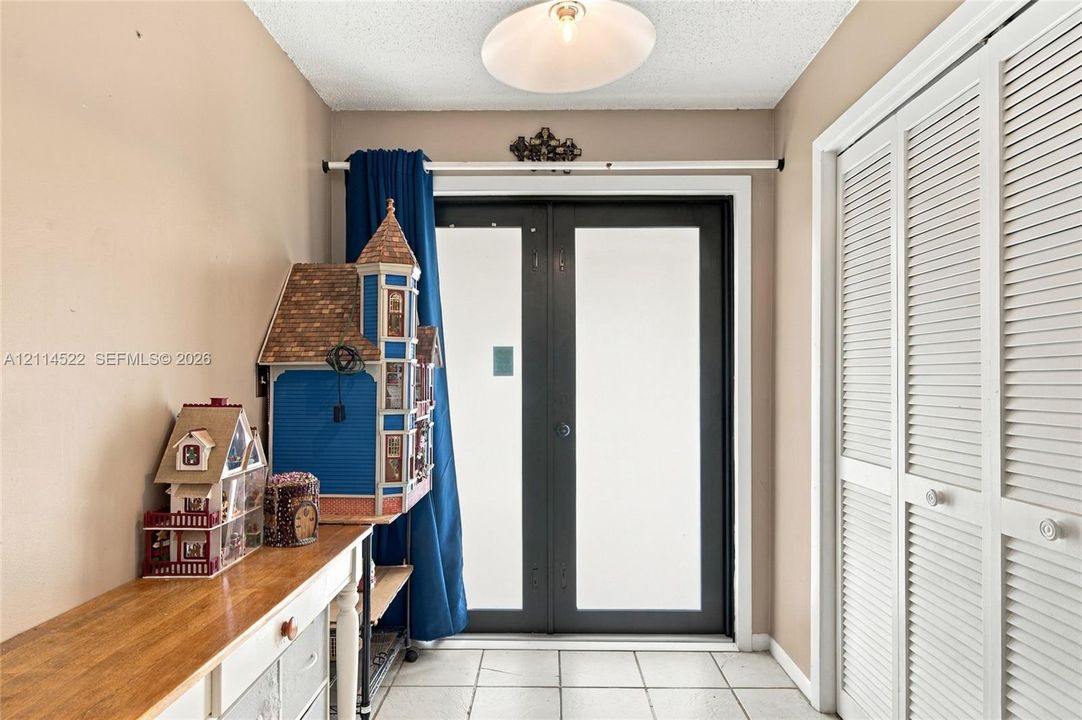 Double-entry doors with opaque glazing, white louvered-style bi-fold closet doors, and ceramic tile flooring