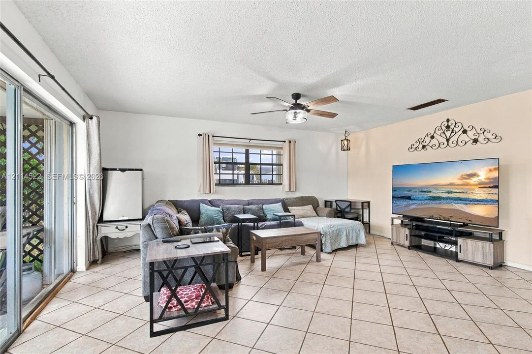 Living area featuring oversized ceramic tile flooring, a multi-blade ceiling fan with integrated lighting, and sliding glass doors with exterior patio access