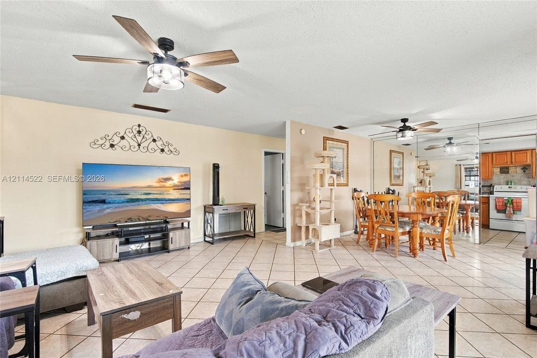 Open-concept main living area featuring diagonal tile flooring, dual ceiling fans, and a floor-to-ceiling mirrored wall