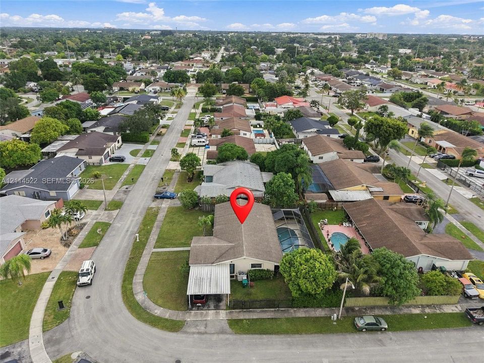 Aerial perspective featuring a single-story residence with a pitched shingle roof, attached covered carport, and enclosed swimming pool area