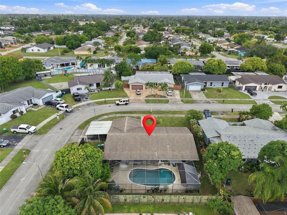 Aerial perspective featuring a shingled roof, screened-in swimming pool enclosure, and covered carport