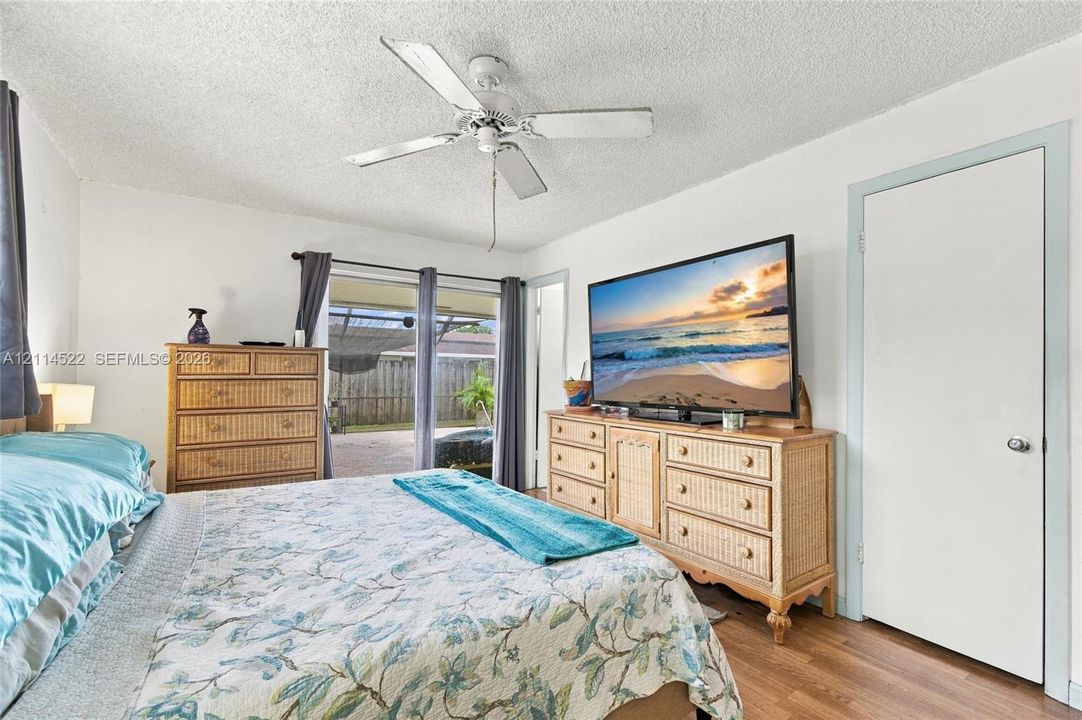 Bedroom featuring wood-finish flooring, a ceiling fan, and glass sliding doors providing exterior access