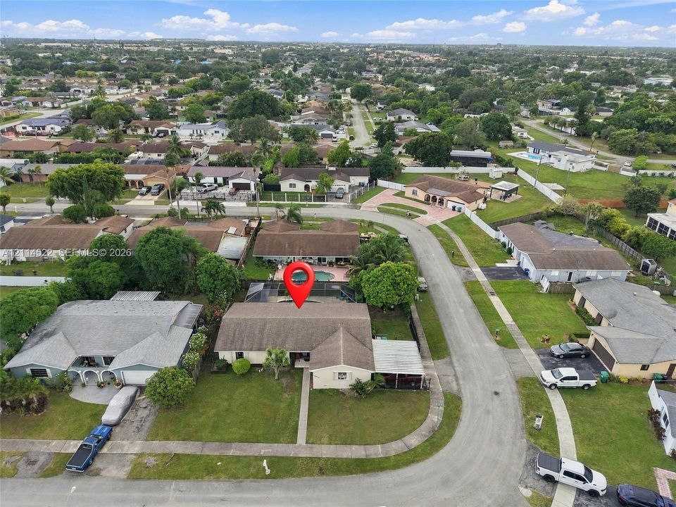 Aerial perspective of a single-story residence featuring a shingled roof, a screened-in rear patio, a private swimming pool, and a manicured front lawn