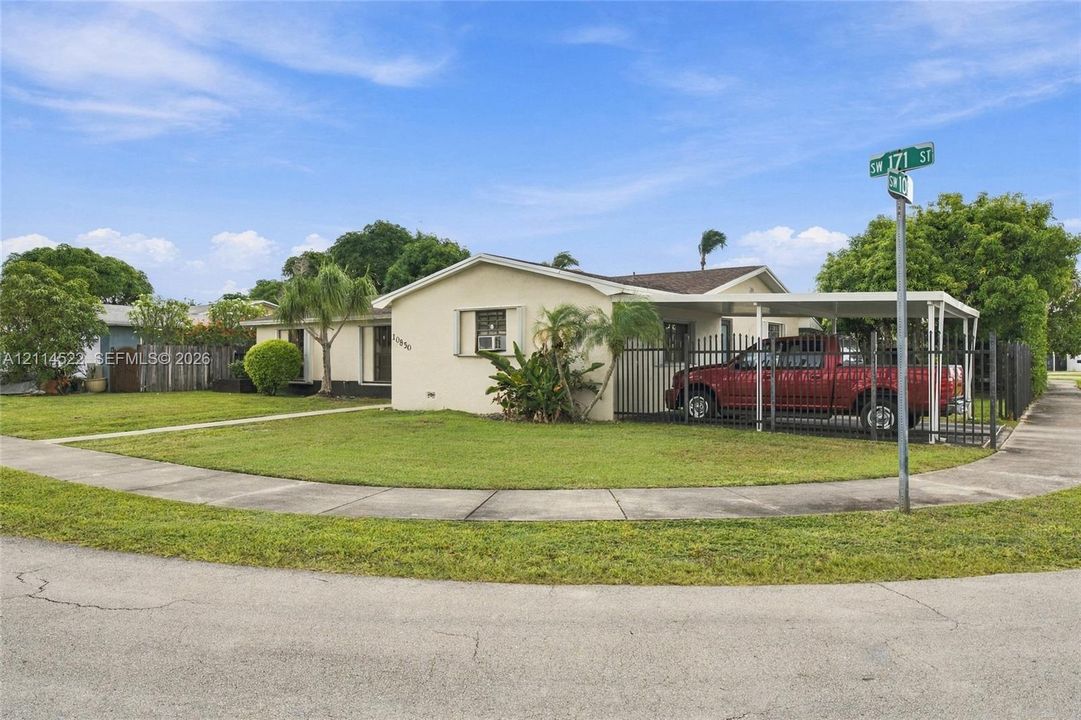 Single-story exterior featuring a light-toned stucco facade, an attached metal-frame carport, and a perimeter metal fence