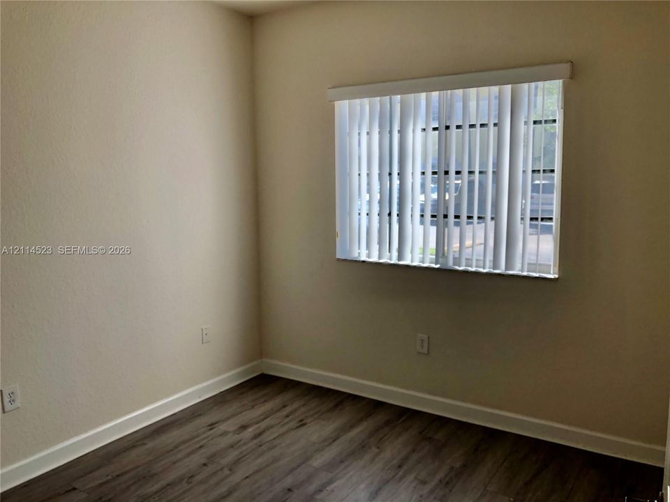 Room featuring wood-finish flooring, neutral wall tones, and a window equipped with vertical blinds